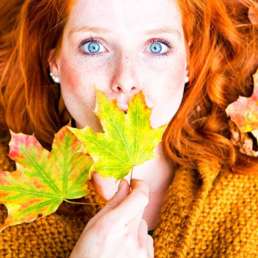 rothaarige Frau mit 2 Blättern vorm Mund