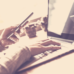 Rechte Hand an der Tastatur des Notebooks mit Smartphone in der anderen Hand