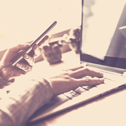 Rechte Hand an der Tastatur beim digitalem Arbeitendes Notebooks mit Smartphone in der anderen Hand